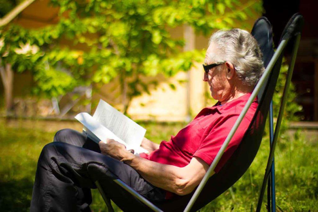 An elderly man enjoying a digital detox by reading a book outdoors in nature, symbolizing relaxation and disconnection from technology