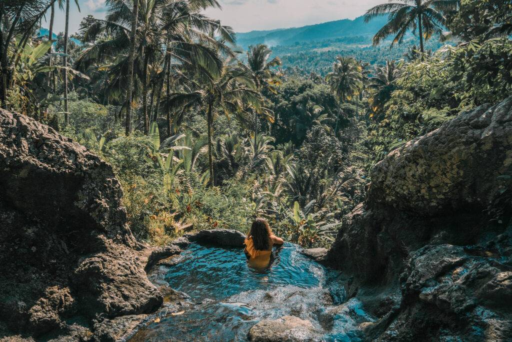 A person enjoying a natural stone pool surrounded by tropical forest, symbolizing digital detox and connection with nature