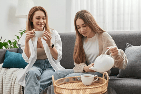 femme assise près d’une fenêtre ouverte, lumière du matin, tasse à la main.